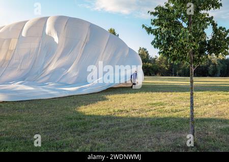 A pilot and a large, white hot air balloon are across in meadow before takeoff. Stock Photo