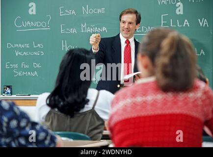 Male Caucasian Spanish language High school teacher standing in front of a blackboard with Spanish written on the board well questioning his students Stock Photo