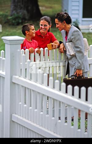 A mother and son talking with they were new neighbor across White Pickett backyard fence Stock Photo