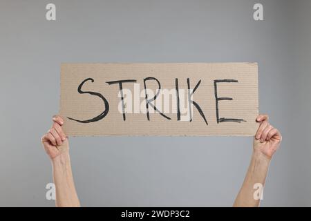 Woman holding cardboard banner with word Strike on grey background, closeup Stock Photo