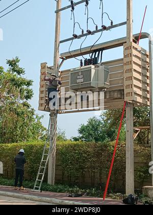 An electrician worker climbs onto an electrical transformer using a ladder for maintenance and repair. Mobile photo. Stock Photo