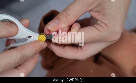 Mom cuts her newborn son's fingernails with small children's scissors. Stock Photo