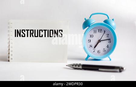 INSTRUCTIONS The word is written in a notepad with a pen and a clock on a white background. Business concept Stock Photo