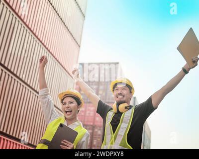 Two Asian engineer raise their hands up cheering for their victory, mission complete , smile to show their happiness in Container Terminal. Stock Photo