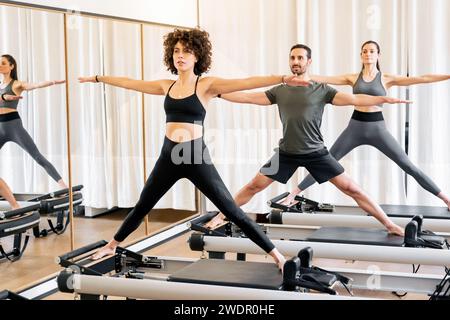 Group of happy young sporty people in activewear with eyes closed relaxing  and deep breathing while standing with namaste in tadasana and meditating  beside black wall in modern yoga studio stock photo