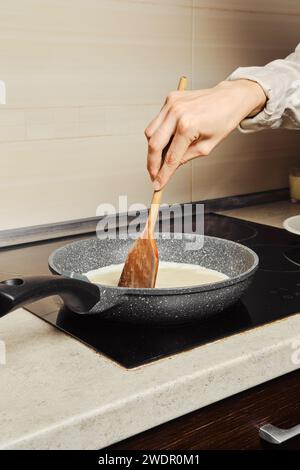 Unrecognizable woman miking scrambled eggs in a frying pan in her kitchen Stock Photo