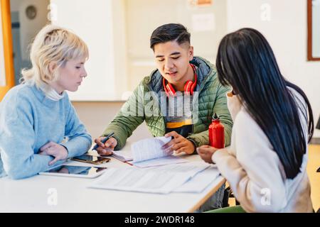 Diverse group of focused students discussing academic work in a classroom environment, exemplifying teamwork and education. Stock Photo