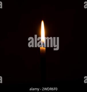 A single burning candle flame or light is glowing on an orange candle on black or dark background on table in church for Christmas, funeral or memorial Stock Photo
