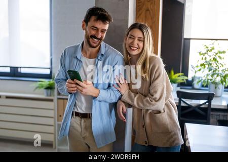 Young happy couple using phone to share social media news at home, doing shopping online. Stock Photo