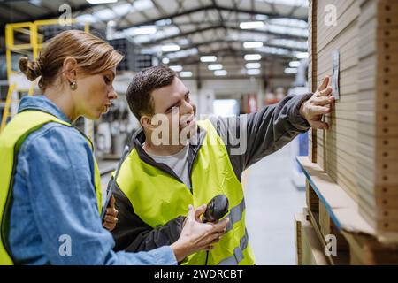 Young man with Down syndrome working in warehouse, female colleague teaching him scan products with scanner. Concept of workers with disabilities Stock Photo