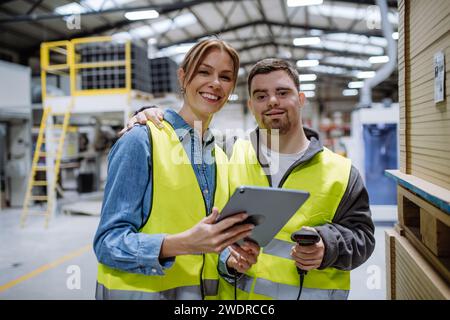 Young man with Down syndrome working in warehouse, female colleague teaching him scan products with scanner. Concept of workers with disabilities Stock Photo