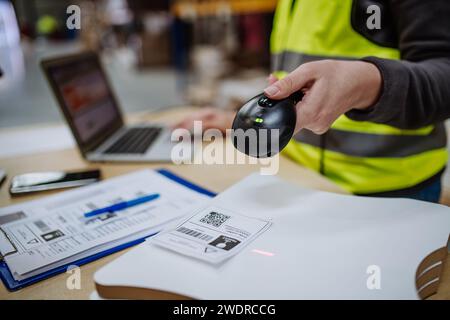 Female warehouse worker holding scanner, scanning the barcodes on products in warehouse, checking in laptop. Warehouse manager using warehouse Stock Photo