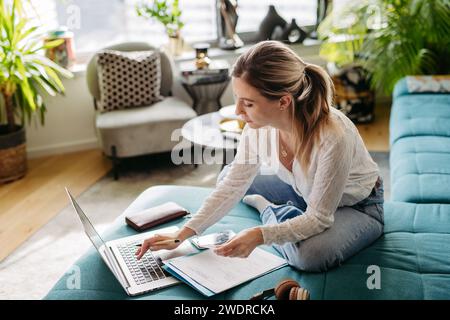 Woman paying bills online, sitting in living room, working on notebook. Online banking, internetbanking at home throught website, app. Stock Photo