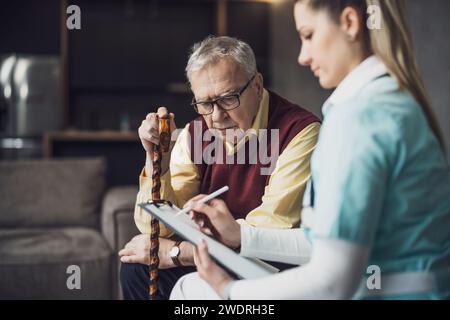 Home doctor is visiting senior man to check his health. Professional caregiver is assisting old man at his home. Stock Photo