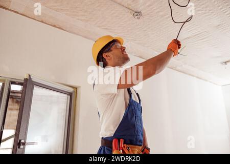 Joyful male electrician repairing electric cable on ceiling Stock Photo