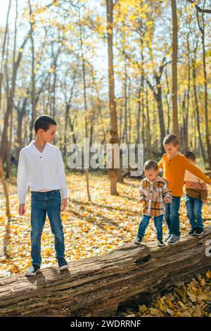 Group of young boys walking across log in forest on a sunny autumn day Stock Photo