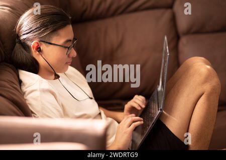 Asian young guy in glasses, headphones preparing for exams at home Stock Photo