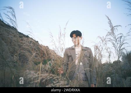Young Chinese man in a trench coat standing among tall grasses Stock Photo
