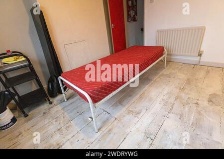 Unmade up single metal framed bed with folding legs and a red mattress in a guest bedroom Stock Photo