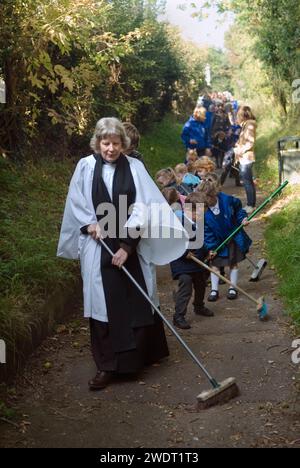 Old Mans Day Braughing, Hertfordshire, the Rev'd Julie Gawthrope sweeping Fleece Lane from the Fleece Inn leading to St Marys the Virgin church with the help of children from Jenyns First School. England  1st October 2015.  UK  2010s HOMER SYKES Stock Photo