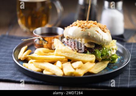 Beef burger topped with cheese with fries and draft beer on a pub or restaurant plate. Stock Photo