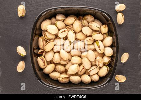 A few tasty pistachios in a black ceramic plate on a slate stone, macro, top view. Stock Photo