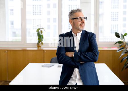 Ambitious mature businessman in formal wear and glasses standing with arms crossed in contemporary office space and looking at the camera, Portrait of purposeful senior ceo manager boss indoor Stock Photo