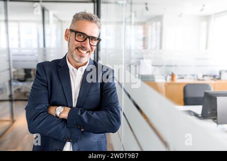 Portrait of confident mature gray-haired businessman standing with arms crossed, male office employee in formal wear, high-skilled expert looking at the camera and smiles, ready for new achivements Stock Photo