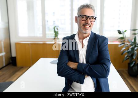 Headshot of high-skilled mature male employee standing with arms crossed in modern office, successful confident 50s businessman wearing eyeglasses, business portrait of senior 60s entrepreneur Stock Photo