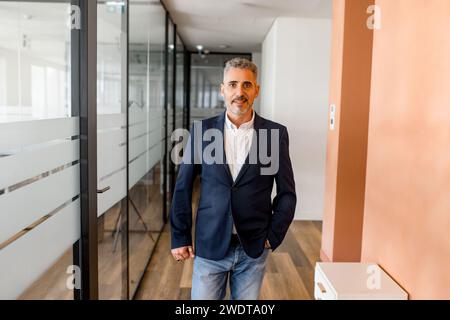 Portrait of a stylish mature businessman standing in the modern office and posing against the glass partition, male employee, manager looking at the camera Stock Photo