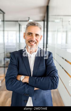 Standing in a bright corridor, a mature businessman presents a portrait of professionalism and accessibility, embodying the dynamism of the modern work environment Stock Photo
