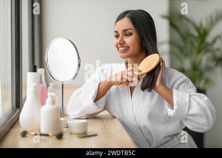 Cheerful indian woman combing beautiful dark long hair at bathroom Stock Photo