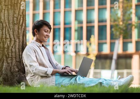 Relaxed young asian guy freelancer working at park Stock Photo