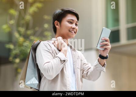 Cheerful chinese man shopping at city center, using smartphone Stock Photo