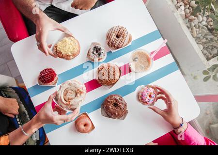 Top view of assorted doughnuts on a table with three hands one male and two females enjoying. Stock Photo