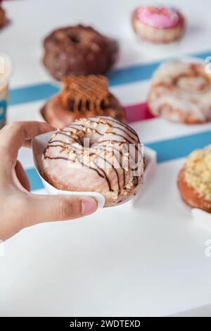 Hand holding peanut butter with chocolate drizzle doughnut in a cafe restaurant environment. Stock Photo
