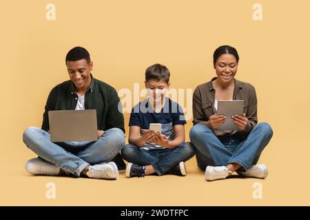 Happy black family of three holding using different electronic devices Stock Photo