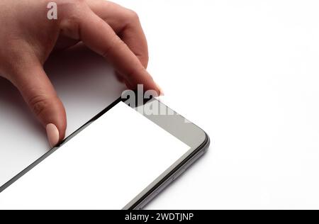 A smartphone with an empty white screen in a woman's hand on a white background. Stock Photo