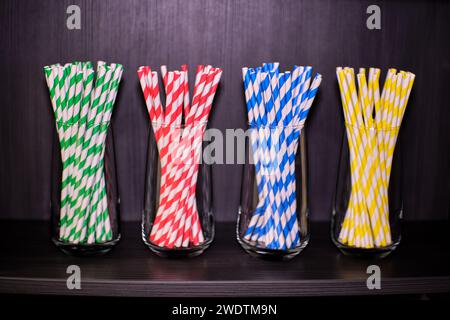 A selection of coloured straws. Green, red, blue and yellow striped straws. In highball glasses on a dark shelf. Stock Photo