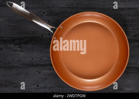 Round fry pan on a weathered black wood texture background. Non-stick, ceramic coated cooking technology. Stock Photo