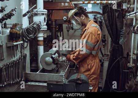 Mechanical engineer working on grinding machine in workshop, with face shield, coverall and gloves. Stock Photo