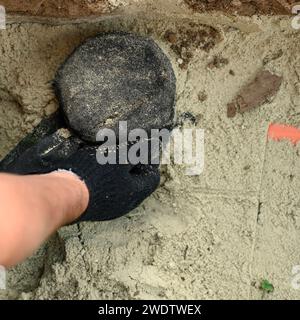 A plumber installs a reinforced orange sewer pipe during site maintenance. Hands of a plumber close-up near a sewer pipe covered with sand. Stock Photo