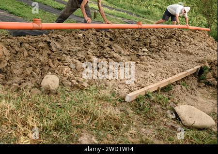 A plumber installs a reinforced orange sewer pipe during site maintenance. Stock Photo