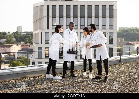 Group of diverse doctors in white medical coats meeting during break outdoors Stock Photo
