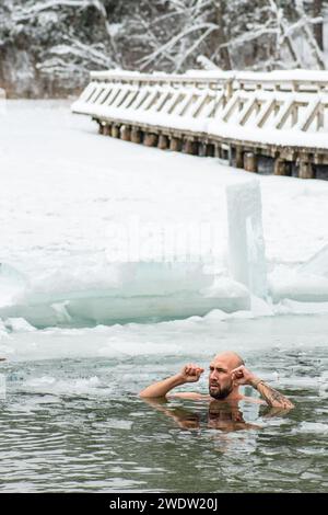 Handsome boy or man ice bathing in the freezing cold water of a frozen lake among ducks. Wim Hof Method, cold therapy, breathing techniques, vertical Stock Photo