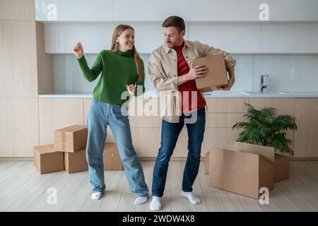Happy couple dancing on kitchen moving in new apartment with cardboard boxes in hands. Stock Photo
