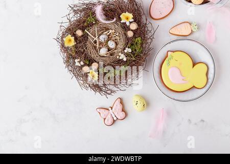 Easter decorated glazed pastel cookies among nest, feathers decorations on the table top view. Stock Photo