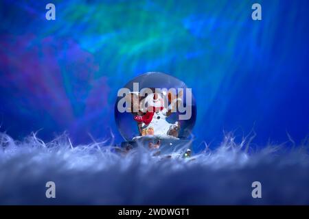 Christmas snowman inside a glass ball with soft fur in the foreground and a colorful background Stock Photo