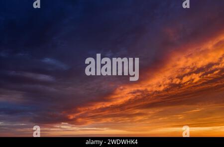 Vibrant sunset sky background with dark clouds illuminated by orange sunlight. Stock Photo