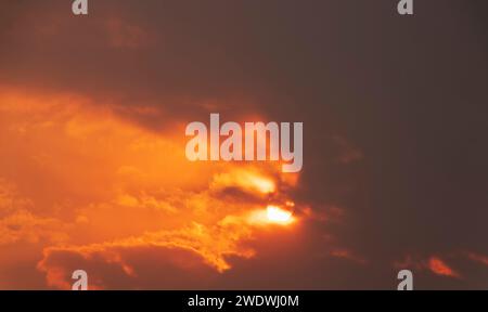 Dramatic sunset sky with bright sun shining through the dark clouds. Stock Photo